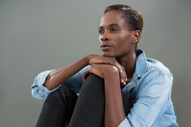 Homme androgyne en chemise en jean posant contre un mur gris