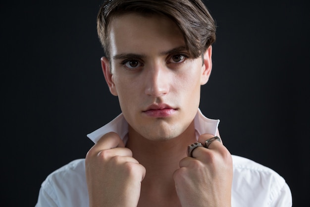 Homme androgyne tenant son collier contre le mur noir