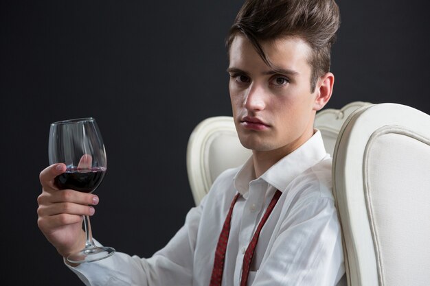 Homme androgyne tenant un verre de vin contre le mur noir