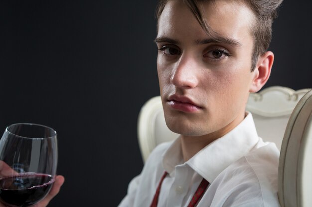 Homme androgyne tenant un verre de vin contre le mur noir