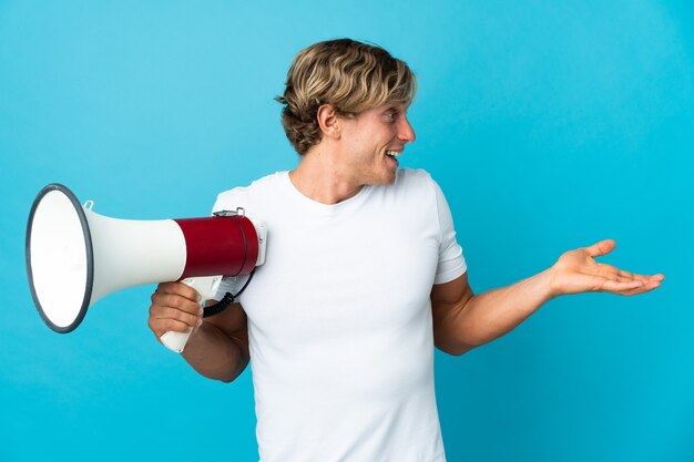 Homme anglais sur bleu tenant un mégaphone et avec une expression faciale surprise