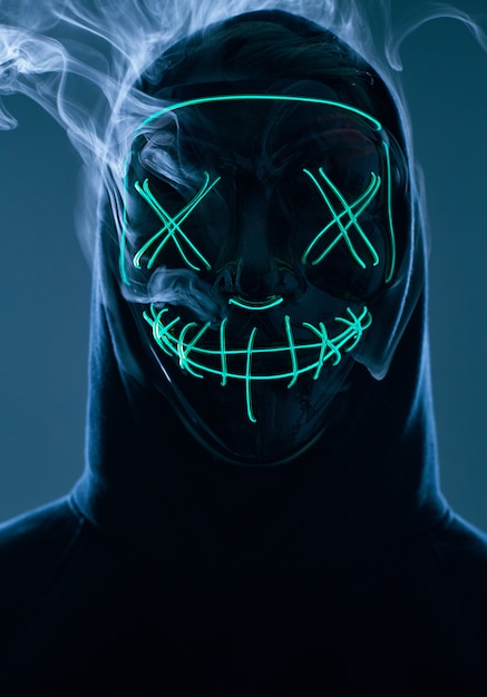 Photo homme anonyme cachant son visage derrière un masque au néon dans une fumée colorée