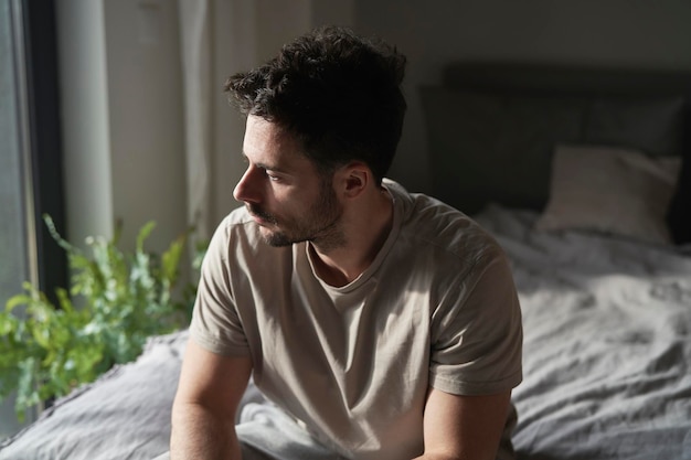 Un homme anxieux à la maison assis sur le lit et détournant le regard