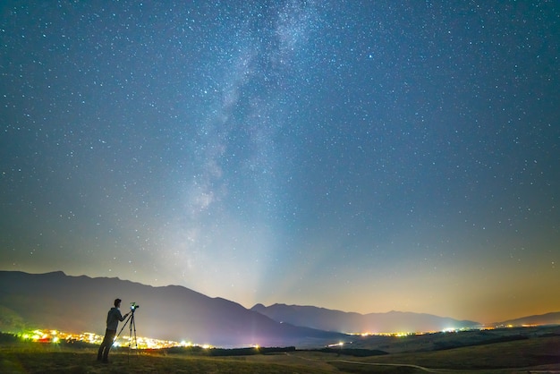 L'homme avec un appareil photo se tient sur le fond du ciel étoilé. la nuit