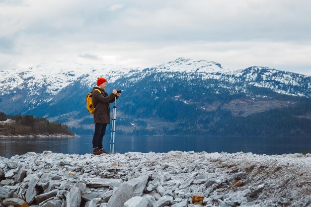 Homme avec appareil photo sur trépied debout sur fond de montagne et un lac fait un paysage photo