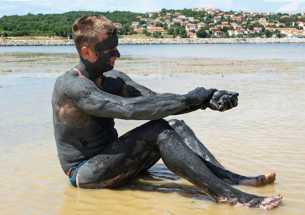 Homme appliquant de l'argile curative noire. Spa de boue sur le rivage