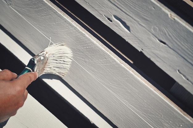 Un homme appliquant de la peinture blanche sur une surface en bois