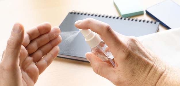 Homme appliquant un spray désinfectant pour les mains sur fond de bureau