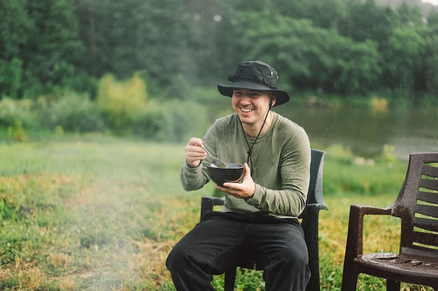 Un homme apprécie la nourriture près du feu Camp de randonnée avec un feu de joie dans la forêt Touriste en loisirs à l'extérieur Style de vie du camping