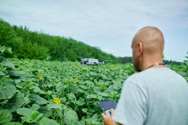 Homme apprenant à piloter son drone chez un homme à l'aide d'un drone volant sur un champ de tournesols