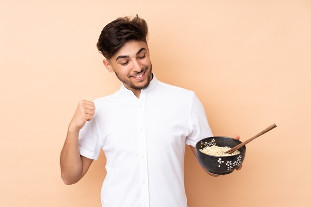 Homme arabe célébrant une victoire tout en tenant un bol de nouilles avec des baguettes
