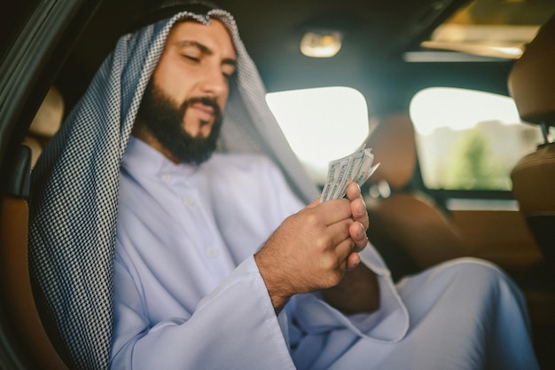 Un homme arabe en costume traditionnel dans une voiture tenant de l'argent