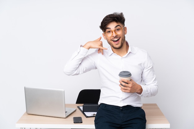 Homme arabe dans un bureau sur un mur blanc faisant un geste de téléphone.