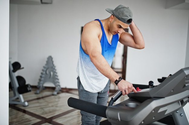 Homme arabe en forme et musclé en cours d'exécution sur tapis roulant dans la salle de gym.