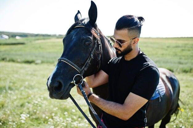 Homme arabe à grande barbe en noir et lunettes de soleil avec cheval arabe.