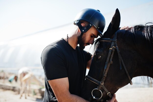 Homme arabe à grande barbe portant un casque noir avec un cheval arabe