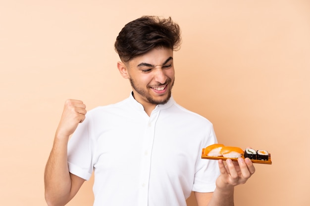 Homme arabe manger des sushis sur mur beige pour célébrer une victoire