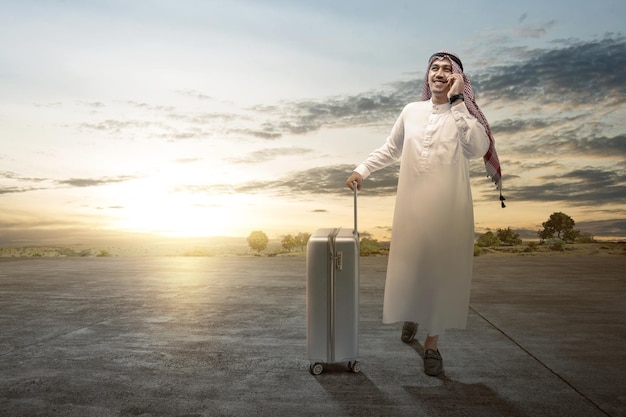 Homme arabe portant un keffieh à l'appel avec une valise pour voyager