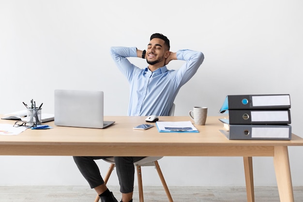 Homme arabe souriant se penchant en arrière assis au bureau