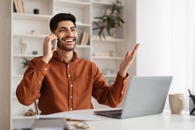 Homme arabe souriant travaillant et parlant au téléphone à la maison