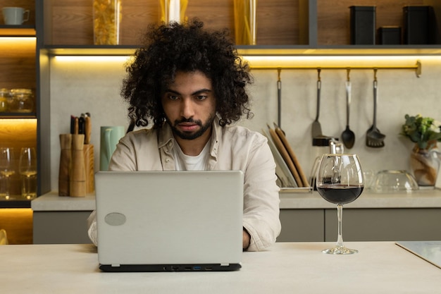 Un homme arabe travaille en ligne sur un ordinateur portable en dégustant un verre de vin