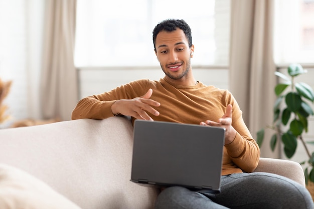 Homme arabe utilisant un ordinateur portable portant des écouteurs assis sur un canapé