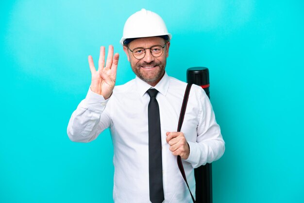 Homme d'architecte d'âge moyen avec casque et tenant des plans isolés sur fond bleu heureux et comptant quatre avec les doigts