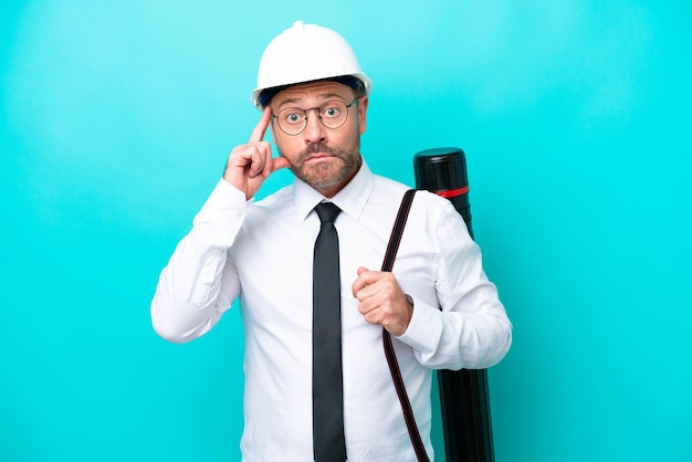 Homme d'architecte d'âge moyen avec casque et tenant des plans isolés sur fond bleu en pensant à une idée