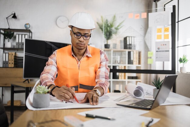 Homme d'architecte compétent assis sur un bureau à l'intérieur à l'aide d'un stylo et d'une règle pour les dessins de projet