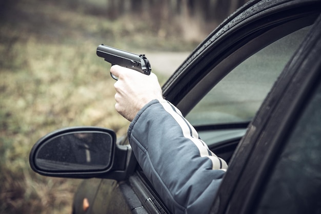 Un homme avec une arme à feu conduisant une voiture, la main d'un homme avec une arme à la main se pencha par la fenêtre de la voiture.