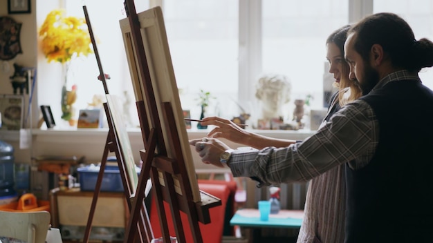 Homme artiste qualifié enseignant à une jeune fille à dessiner des peintures et expliquant les bases dans un studio d'art