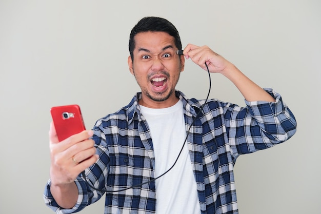 Photo homme asiatique adulte criant fou en branchant des données de câble du téléphone portable à sa tête