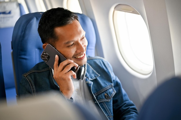 Un homme asiatique adulte heureux est sur le vol vers sa ville natale en train de parler au téléphone avant de décoller