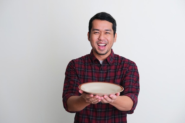 Homme asiatique adulte montrant une expression enthousiaste tout en tenant une assiette vide