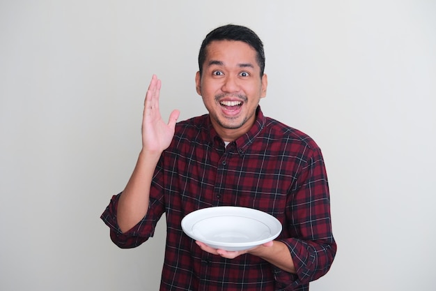 Homme asiatique adulte montrant une expression excitée tout en tenant une assiette vide