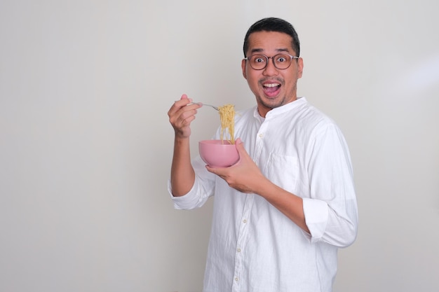 Homme asiatique adulte montrant une expression surprise en mangeant des nouilles
