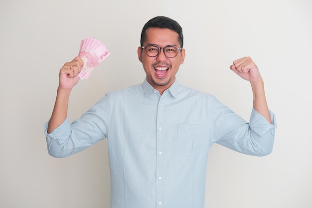 Homme asiatique adulte montrant son muscle biceps avec une main tenant du papier-monnaie