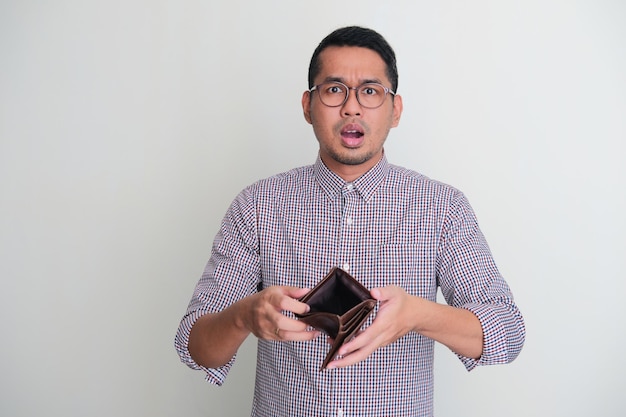 Photo homme asiatique adulte montrant son portefeuille vide avec une expression inquiète