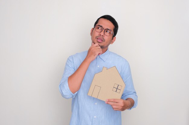 Homme asiatique adulte pensant à quelque chose tout en tenant un carton en forme de maison