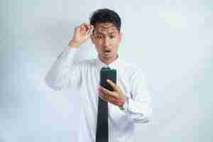Photo un homme asiatique adulte regarde son téléphone portable qu'il tient avec une expression surprise.