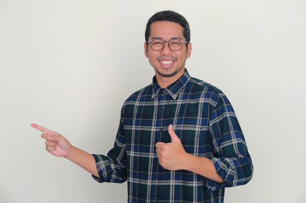 Photo homme asiatique adulte souriant à la caméra et lève le pouce tout en pointant vers le côté droit