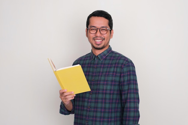 Un homme asiatique adulte souriant avec confiance tout en tenant un livre.