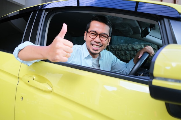 Homme asiatique adulte souriant heureux et donnant le pouce de l'intérieur de la fenêtre du siège du conducteur de voiture