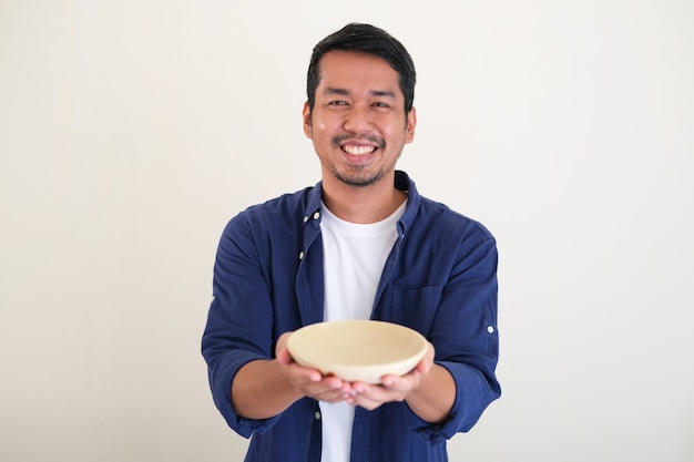 Photo homme asiatique adulte souriant heureux tout en montrant un bol à manger vide