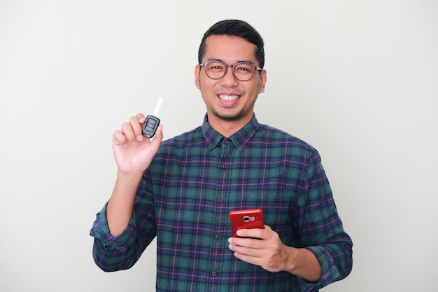 Homme asiatique adulte souriant heureux tout en tenant un téléphone portable et en montrant une clé de voiture