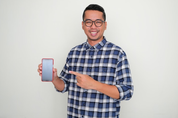 Homme asiatique adulte souriant et pointant vers l'écran vierge du téléphone portable qu'il tient