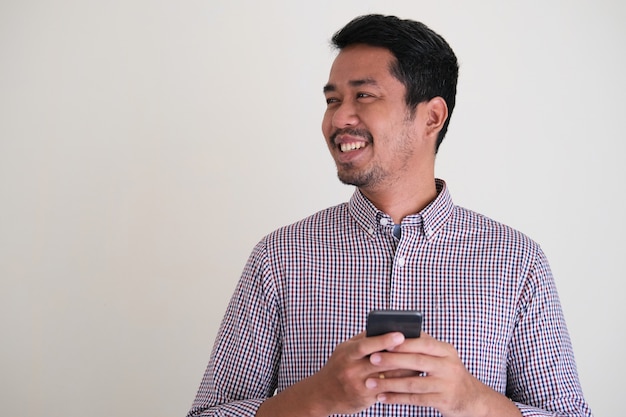 Homme asiatique adulte tenant un téléphone portable tout en souriant amicalement à ses côtés