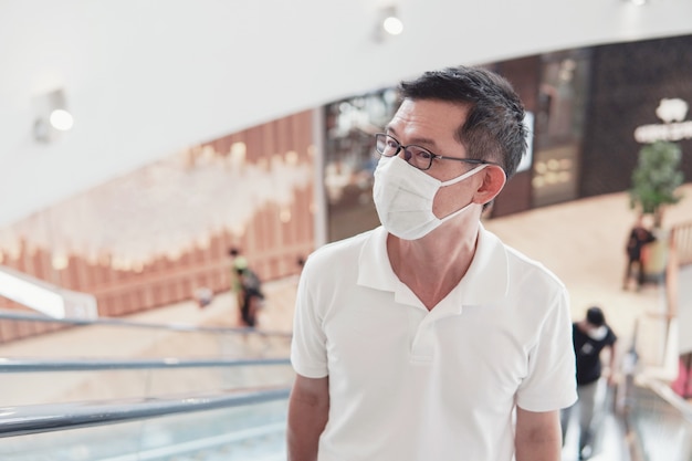 Homme asiatique d'âge moyen portant des lunettes et un masque médical dans un centre commercial, épidémie de coronavirus de Wuhan, pollution de l'air et concept de santé