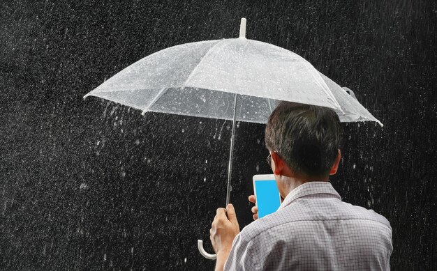 Homme asiatique d'âge moyen tenant son parapluie et son téléphone sous la pluie la nuit