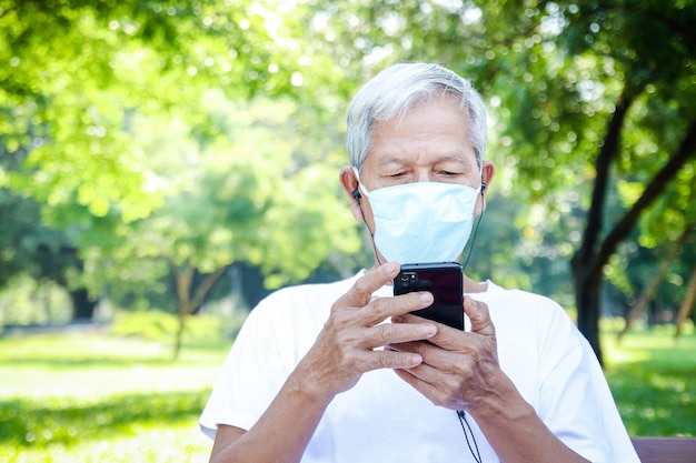 Un homme asiatique âgé portant un masque utilise un smartphone